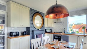A modern kitchen with white cabinets, a round mirror, a copper pendant light, and a dining table set for six. - Highpoint Lodge (Lyme Regis)