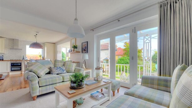 A spacious living room with a sofa set, a coffee table, and a view of the garden through large windows. - Highpoint Lodge (Lyme Regis)