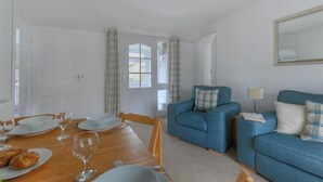 A room with a dining table set for two, a blue sofa, and a mirror on the wall. - Hatchett Top Flat (Lyme Regis)