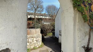 A narrow pathway leading through a white wall with a stone wall on one side and a wooden fence on the other. - Hatchett Top Flat (Lyme Regis)