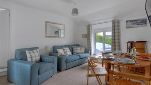 A living room with two blue sofas, a dining table set with plates and glasses, and a wooden cabinet. - Hatchett Top Flat (Lyme Regis)