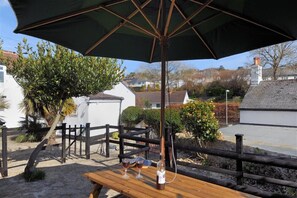 An outdoor seating area with a wooden table and an umbrella, surrounded by a wooden fence and greenery. - Hatchett Top Flat (Lyme Regis)