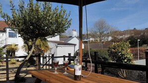 An outdoor seating area with a wooden table, a bottle, and glasses, surrounded by a wooden fence and various plants. - Hatchett Top Flat (Lyme Regis)