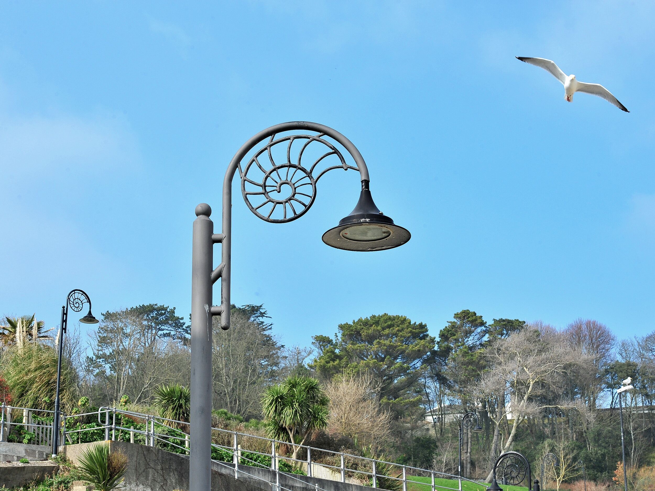 Una farola de diseño peculiar, una valla metálica y un ave volando.