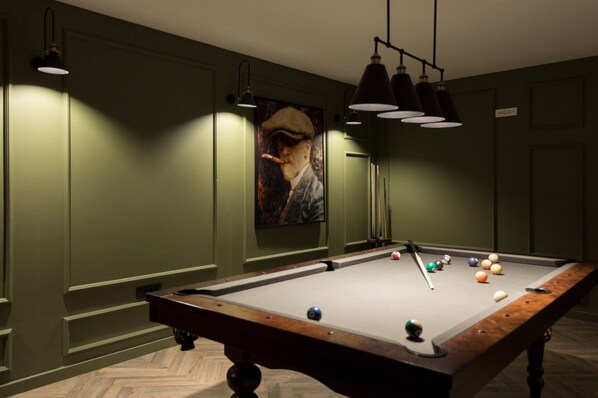 A pool table with balls and cues, green walls, and pendant lighting.