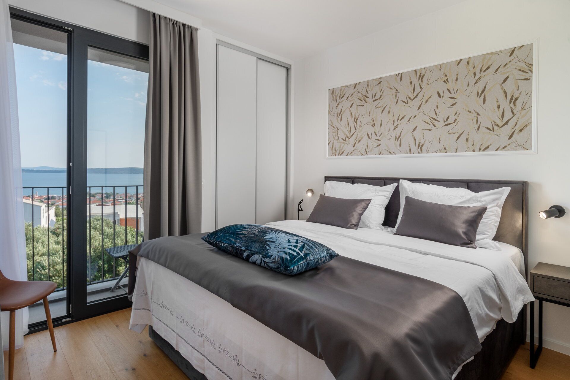 Un dormitorio con una cama grande, vistas a la ciudad desde un balcón y una pared con diseño de hojas.