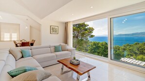 A modern living room with a large window offering a scenic view of the sea and greenery. - Luxury Villa Aerius with Pool (Pučišća)