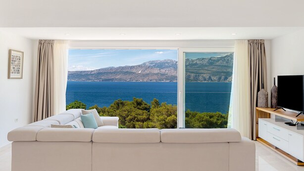 A modern living room with a white sofa, a flat-screen TV, and a view of the sea and mountains. - Luxury Villa Aerius with Pool (Pučišća)