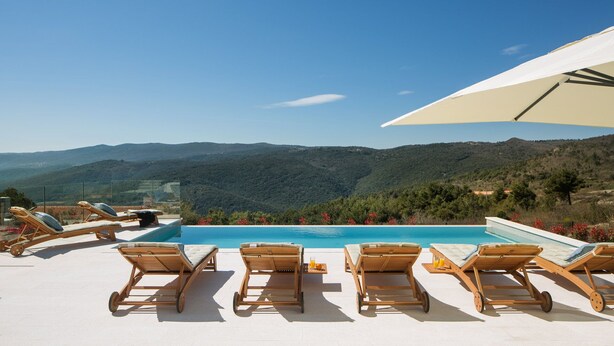 A poolside area with lounge chairs and a view of a mountain range.