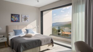 A modern bedroom with a large window, a bed with blue and white bedding, and two abstract paintings on the wall.