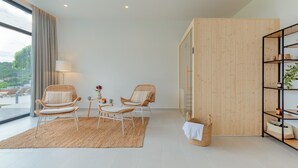 A modern living room with two wicker chairs, a small table, a woven rug, and a wooden bookshelf.
