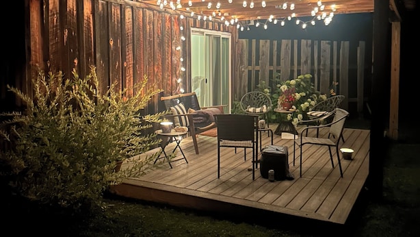 Una terraza de madera con asientos exteriores, luces colgantes y una planta en maceta.
