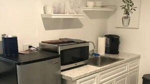 Cocina compacta con microondas integrado, refrigerador de acero inoxidable, pileta y mesón con cafetera.