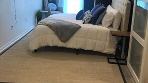 Un dormitorio con cama, televisor montado en la pared y ventana con cortinas.