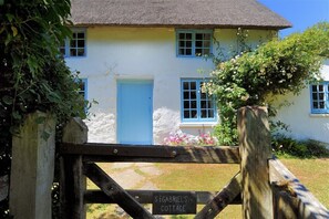 A cottage with a blue door and windows, surrounded by greenery and a wooden gate. - St Gabriels Cottage (Bridport)