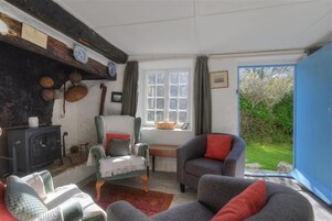 Una sala de estar acogedora con chimenea, un sillón verde, un sofá gris y vistas al jardín a través de un ventanal grande.