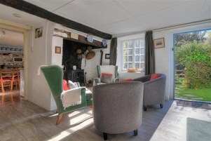 Una sala de estar acogedora con chimenea, sillones verdes y grises, y vistas al jardín.