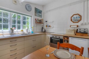 Una cocina con una mesa de madera, un reloj y un ventanal con vistas a follaje.