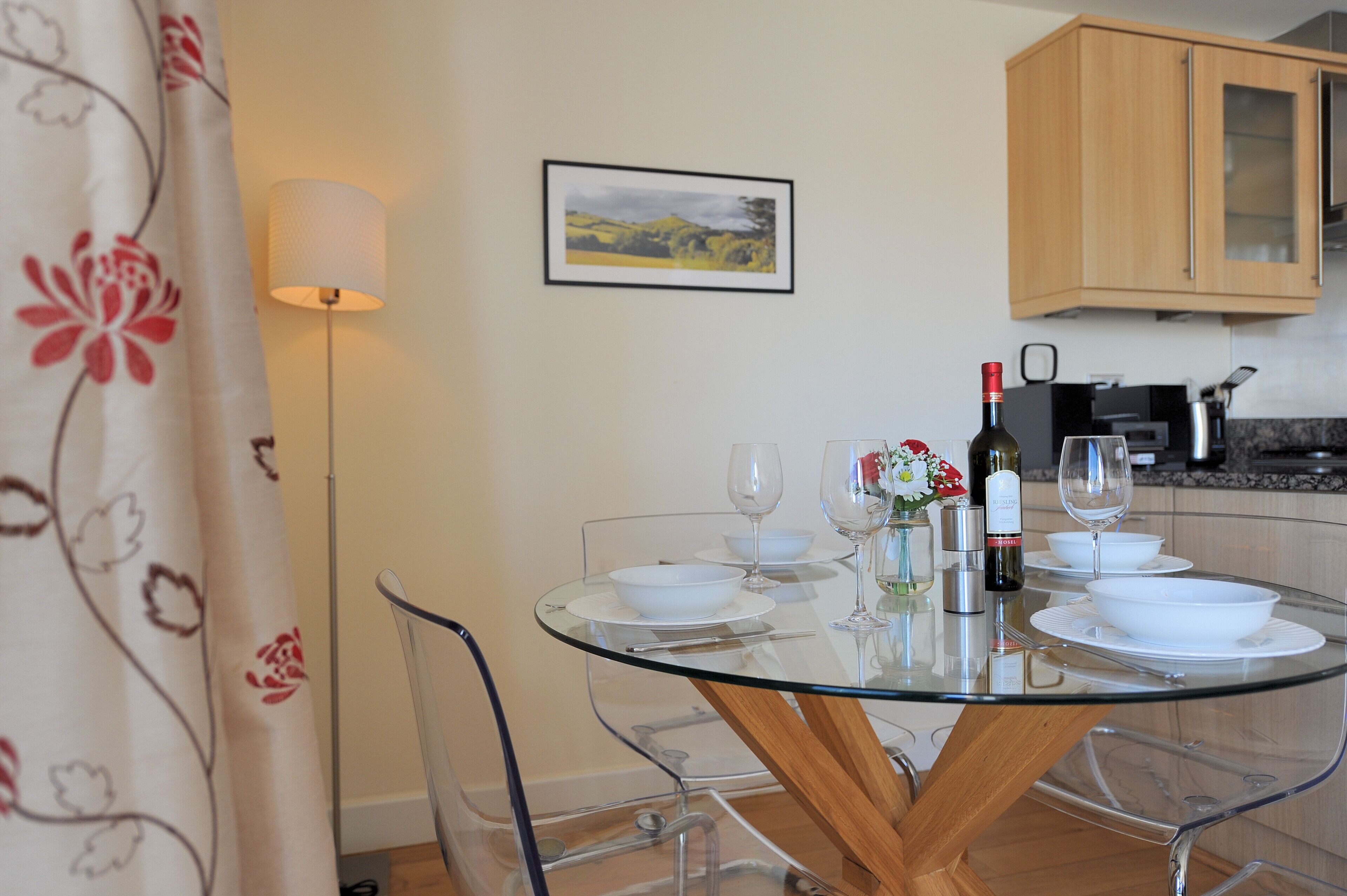 A dining area with a glass table, white plates, wine glasses, and a bottle of wine.