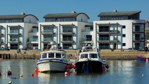A marina with boats docked in front of modern buildings with balconies. - Harbour View (Bridport)