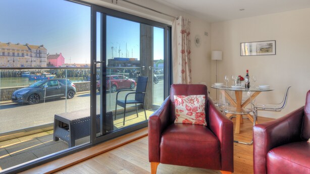 A modern room with a large sliding glass door leading to a balcony, a dining table with chairs, and a red leather sofa. - Harbour View (Bridport)