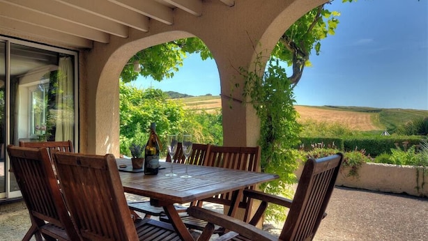 Un patio al aire libre con una mesa y sillas de madera, una botella de vino y copas.