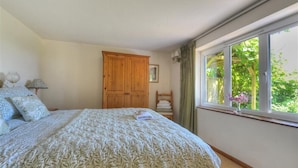 Un dormitorio con una cama grande, un armario de madera, una ventana con vistas a la vegetación y una mesita de noche con lámpara.