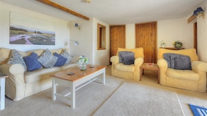 Una sala de estar con un sofá color beige, dos sillones, una mesita de centro y un cuadro en la pared.