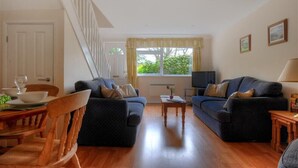 Una sala de estar con dos sofás, una mesa de comedor con sillas, un televisor y una escalera.