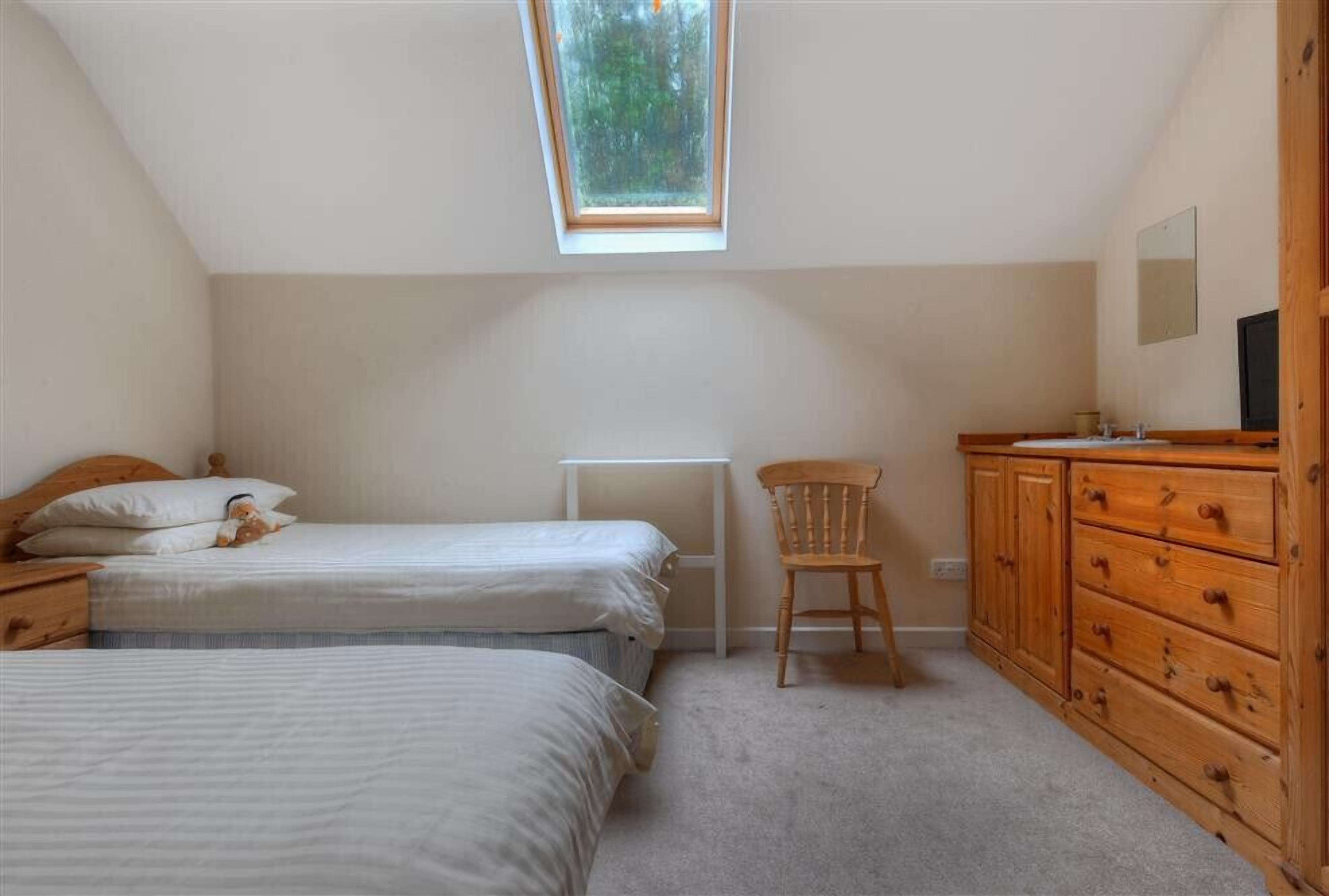 Un dormitorio con dos camas, un aparador de madera, una silla y un tragaluz.