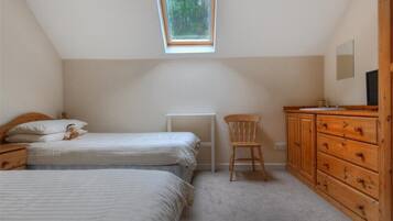 Un dormitorio con dos camas, un aparador de madera, una silla y un tragaluz.