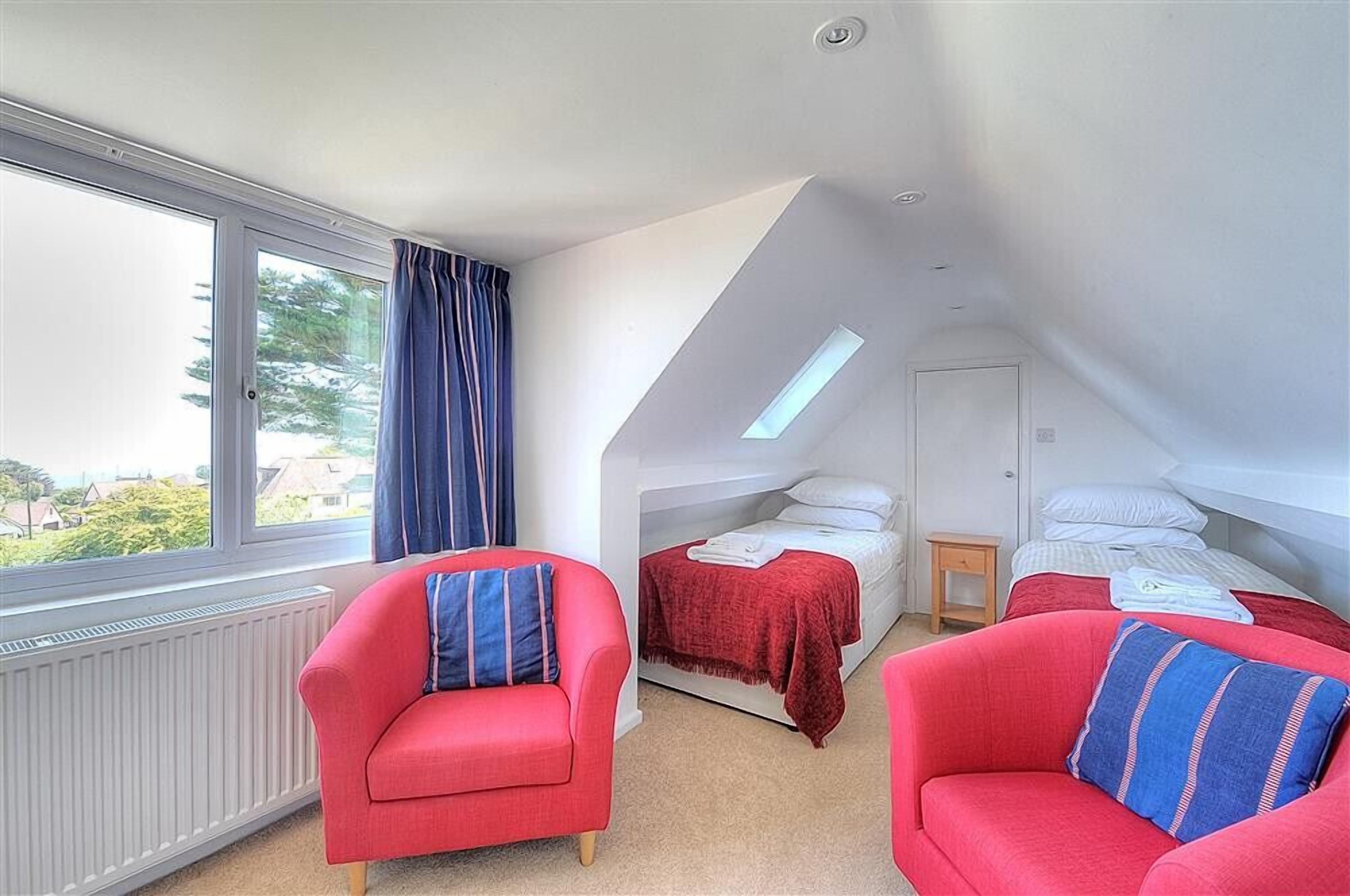 Ein Schlafzimmer mit Dachfenster, zwei roten Sofas, einem Bett mit roter Decke und Blick auf Grünflächen.