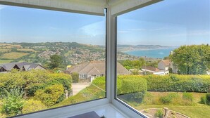 Une pièce dotée d’une grande fenêtre donnant sur un paysage côtier, avec des maisons et de la végétation.