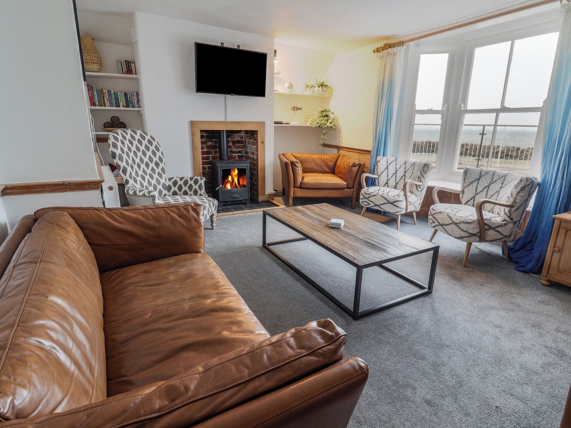 Una sala de estar con sofá de cuero, sillones estampados, una mesa de centro, chimenea, televisor y vistas a través de una ventana.