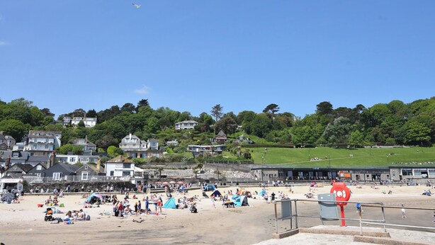 A beach with people sunbathing and swimming, a lifeguard tower, and houses in the background. - Captains House (Lyme Regis)