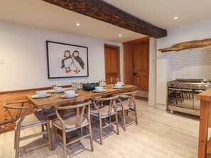 Un coin repas avec une table en bois, dressée pour quatre personnes, entourée de chaises en osier. Un tableau encadré représentant des oiseaux est accroché au mur au-dessus de la table.