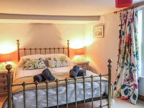 Un lit bien fait, avec un cadre en métal, deux lampes de chevet et un rideau à motifs floraux.