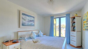 A bedroom with a bed, a nightstand, a bookshelf, and a window with curtains. - Sandstones (Bridport)