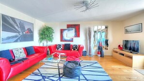 A modern living room with a red sofa, a glass coffee table, and a TV on a wooden stand. - Sandstones (Bridport)