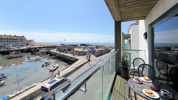 A balcony with a table set for dining, overlooking a harbor with boats and a pier. - Sandstones (Bridport)