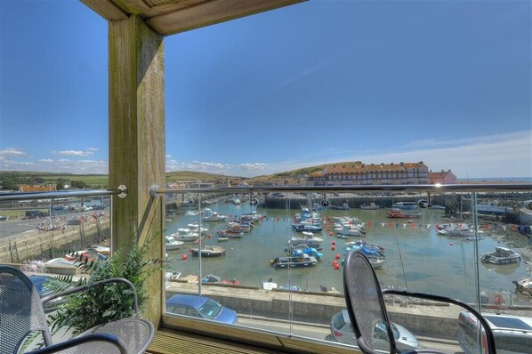 A balcony with a view of a marina filled with boats, a distant building, and a clear sky. - Sandstones (Bridport)