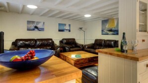 A living room with leather sofas, a wooden coffee table, and a bowl of fruit. There are paintings on the wall and a cabinet with a bottle and glasses on the counter. - The White House (Bridport)