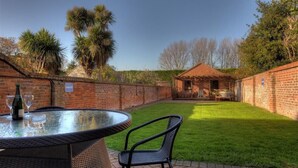 A patio with a round glass table and two chairs, a brick wall, and a small brick building in the background. - The White House (Bridport)