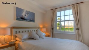 A bedroom with a large bed, two bedside tables, a nightstand, a window with curtains, and a painting on the wall. - The White House (Bridport)