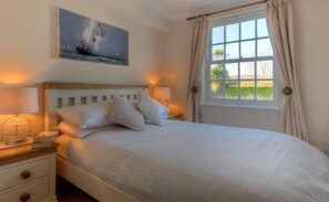 Un dormitorio con una cama grande, dos mesitas de noche, una mesita auxiliar, una ventana con cortinas y un cuadro en la pared.