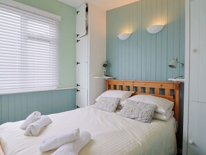 A bedroom with a bed, two bedside lamps, a window with blinds, and a wardrobe. - 1 Wellhayes (Lyme Regis)