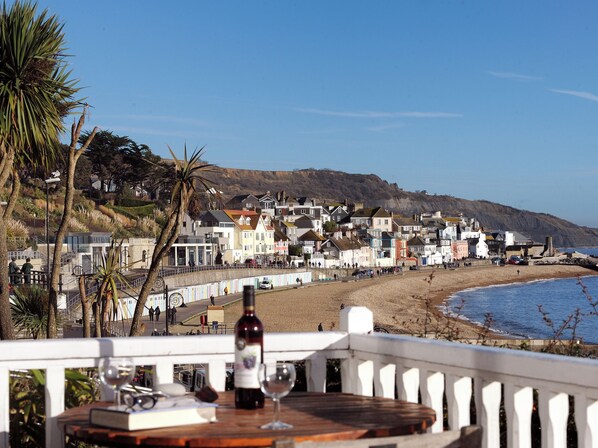 A seaside town with a beach, a white fence, and a table with a bottle and glass. - 1 Wellhayes (Lyme Regis)