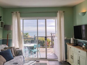 A room with a sofa, a television, a table with chairs, and a sliding glass door leading to an outdoor area with a view of the sea. - 1 Wellhayes (Lyme Regis)