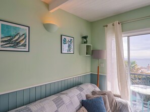 A room with a bed, a wall-mounted shelf with a plant, a framed artwork, and a window with a view. - 1 Wellhayes (Lyme Regis)