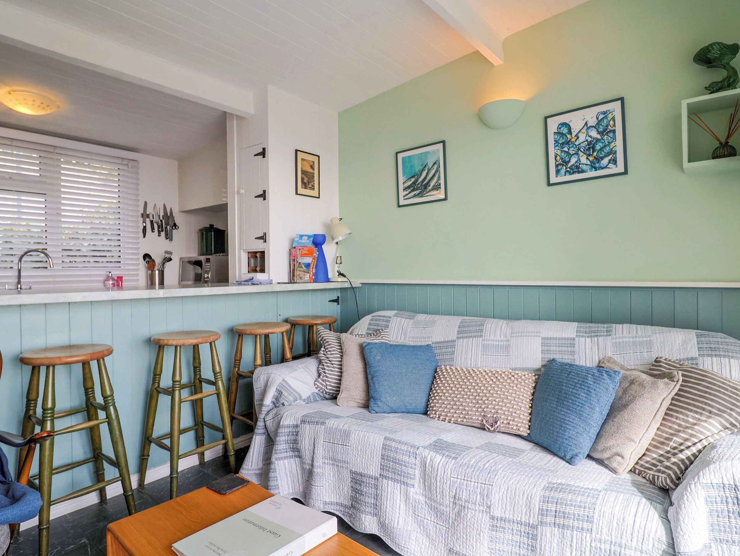 Una sala acogedora con un sofá, taburetes de bar y una zona de cocina con ventanal.